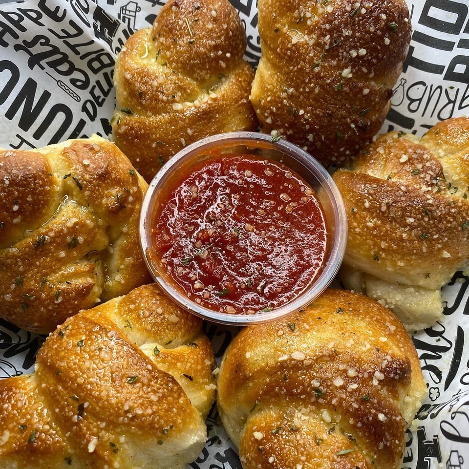 Garlic knots with parmesan and herbs, arranged around a small cup of marinara sauce.