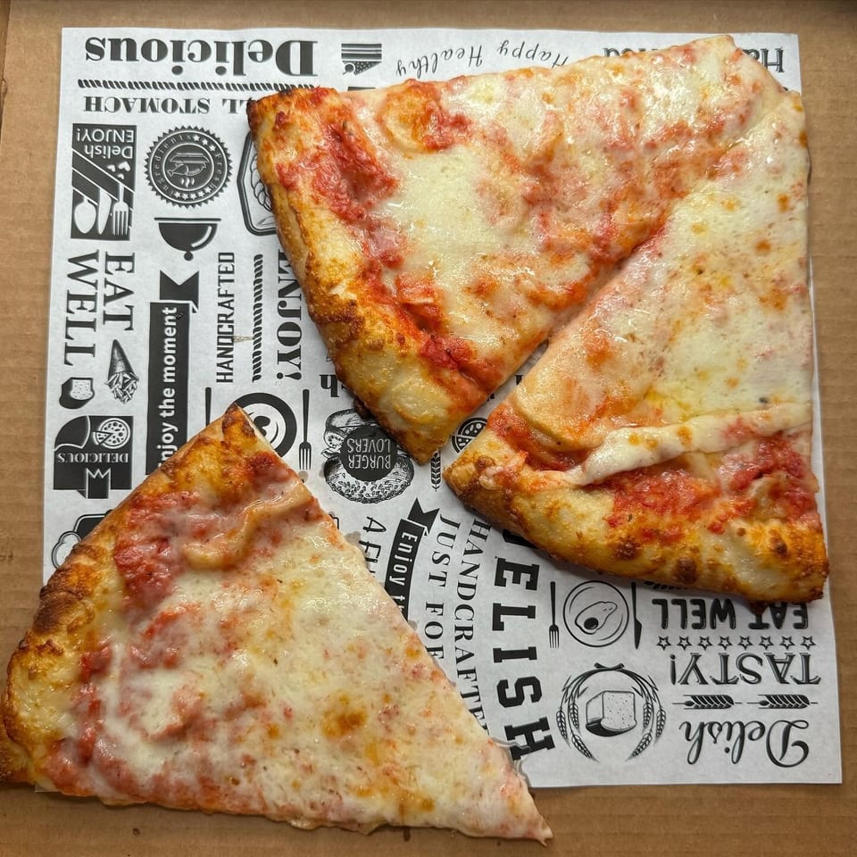 Three slices of cheese pizza with tomato sauce on branded deli paper in a cardboard box.