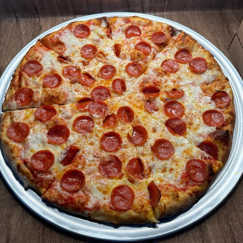 A whole pepperoni pizza, sliced into eight pieces, on a silver pizza pan.