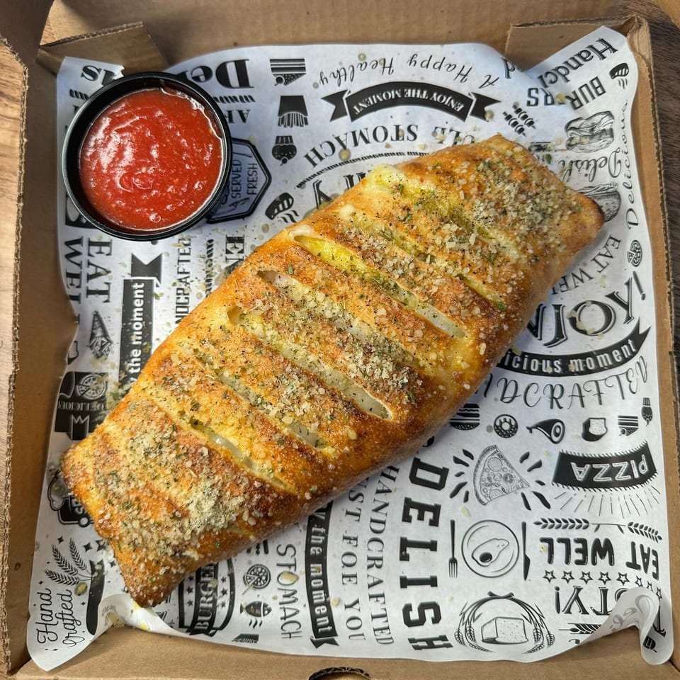 Golden-brown calzone with herbs and parmesan, served with a side of marinara sauce in a box.