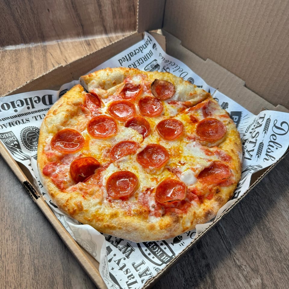 A pepperoni pizza with melted cheese and tomato sauce in a cardboard box lined with branded paper.